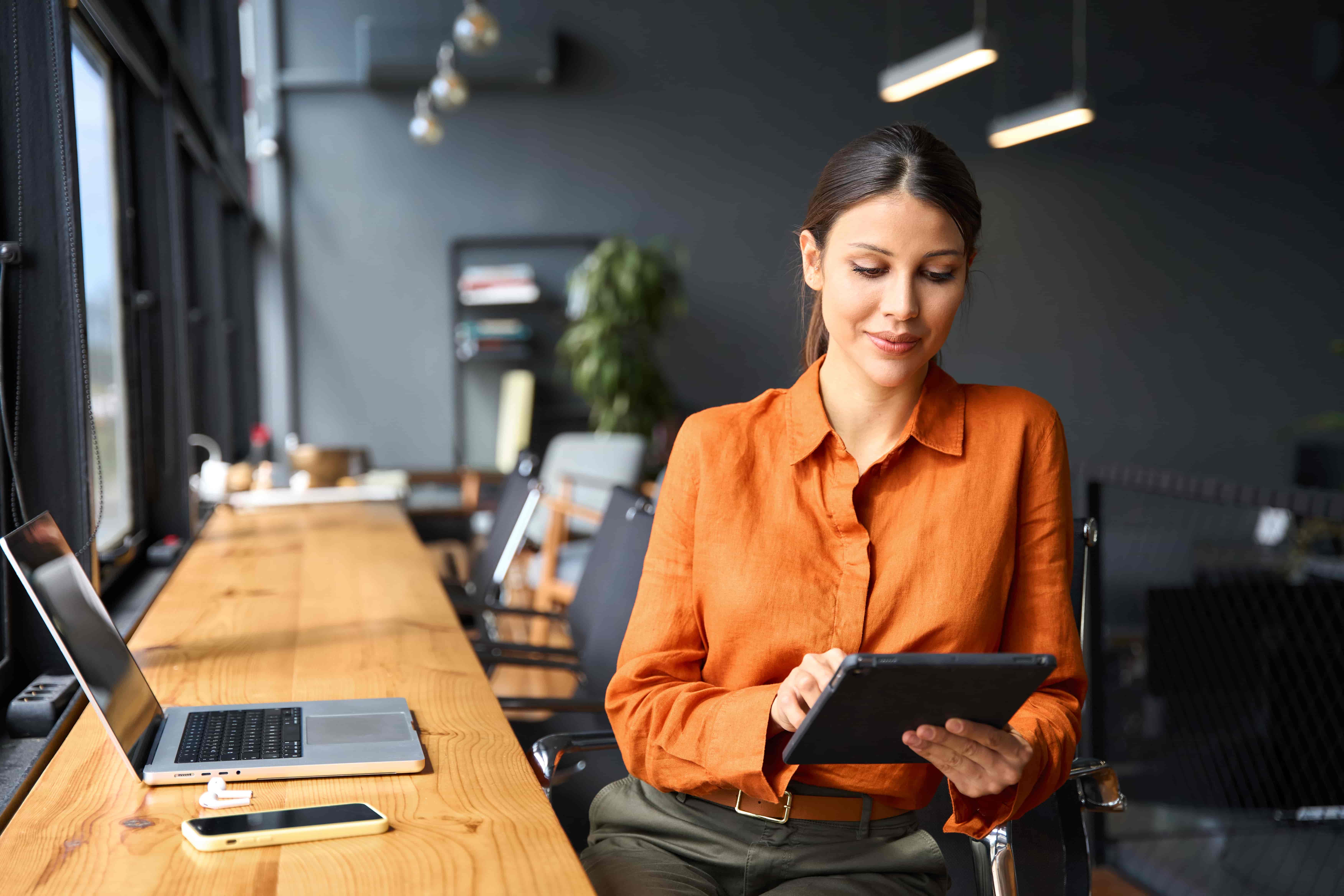Successful smiling latin hispanic young woman using pad computer for business app